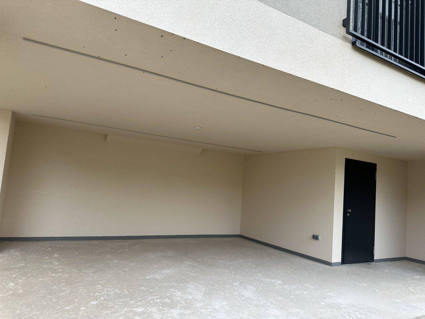 Überdachter Bereich unter dem Gebäude, möglicherweise ein Carport oder Abstellplatz, mit einer schwarzen Tür.
