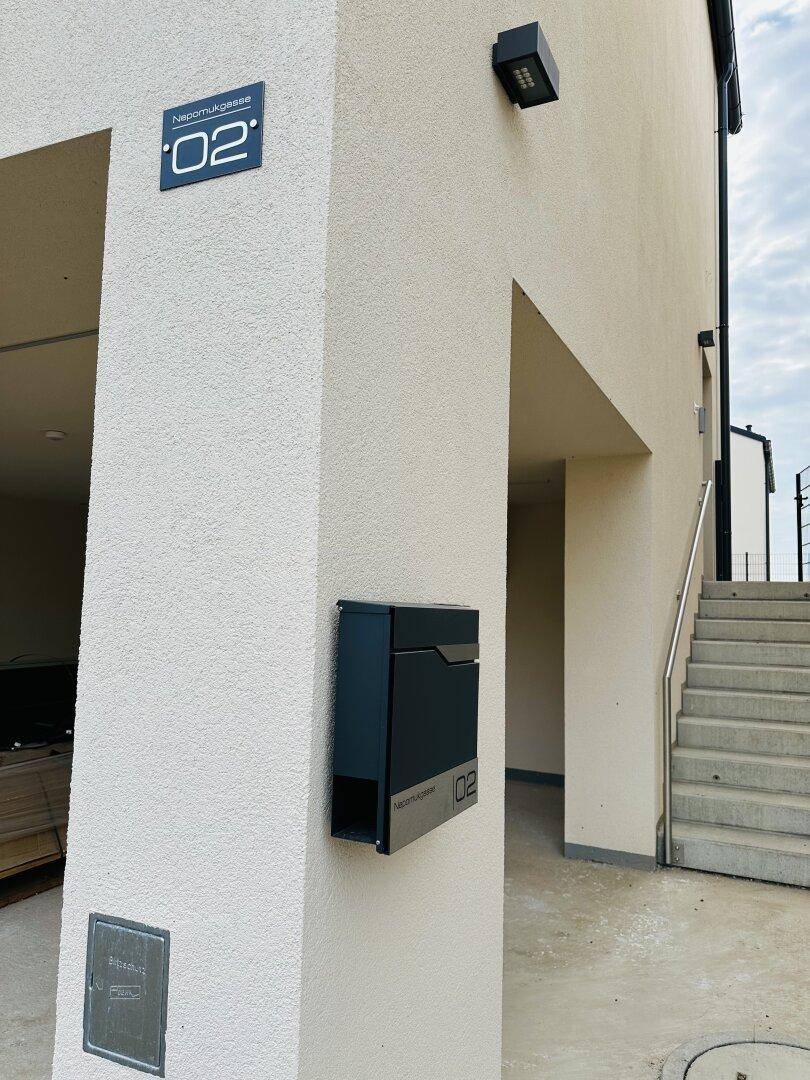 Eingangsbereich eines modernen Reihenhauses mit Hausnummer, Briefkasten und Außenbeleuchtung.