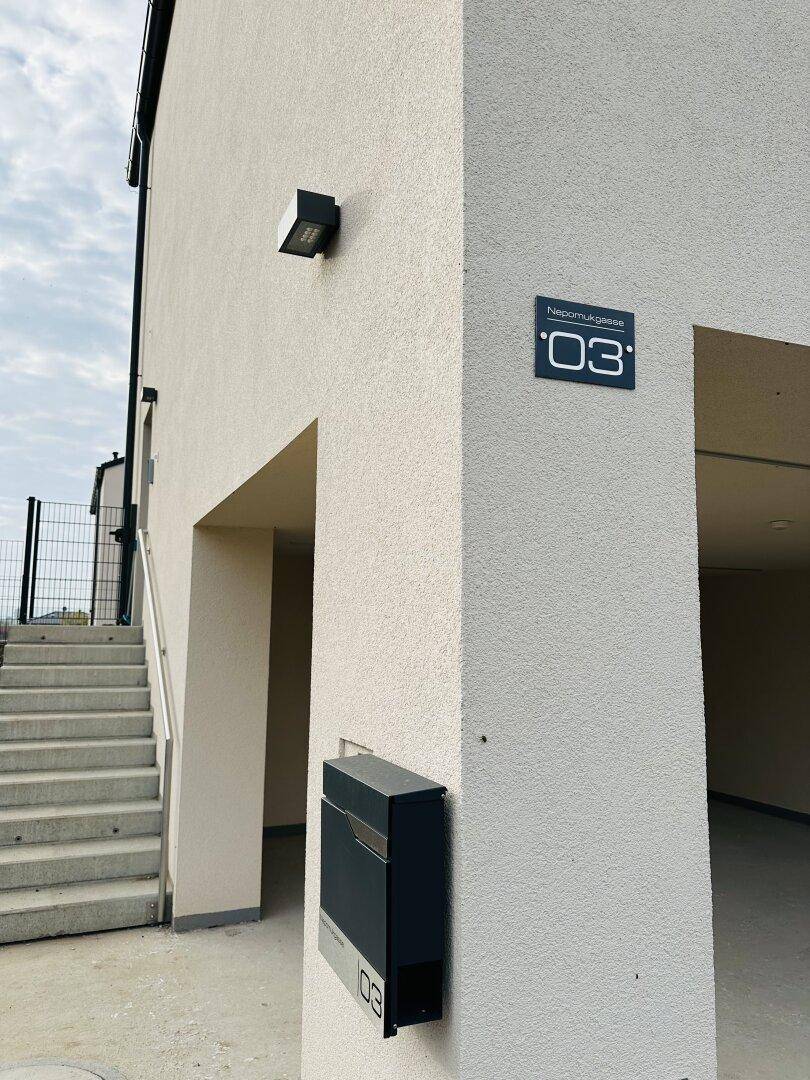 Eingangsbereich eines Neubaus mit moderner Hausnummer und Briefkasten an der Fassade.