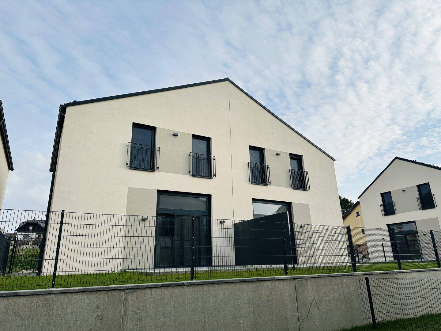 Modernes Reihenhaus mit kleiner Gartenfläche und Zaun, umgeben von Grün.