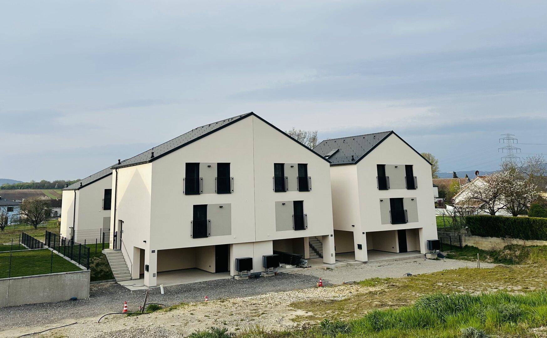 Moderne Neubauhäuser mit schlichter Architektur und dunklen Dächern in ländlicher Umgebung.
