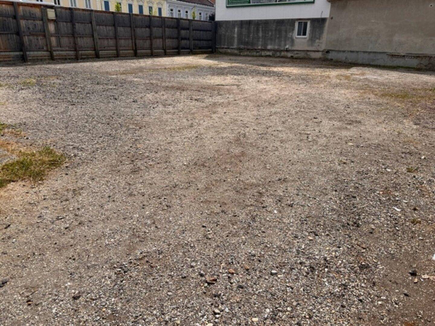 Weitläufiges Kiesgrundstück mit angrenzender Gebäudewand und Holzzaun im Hintergrund.