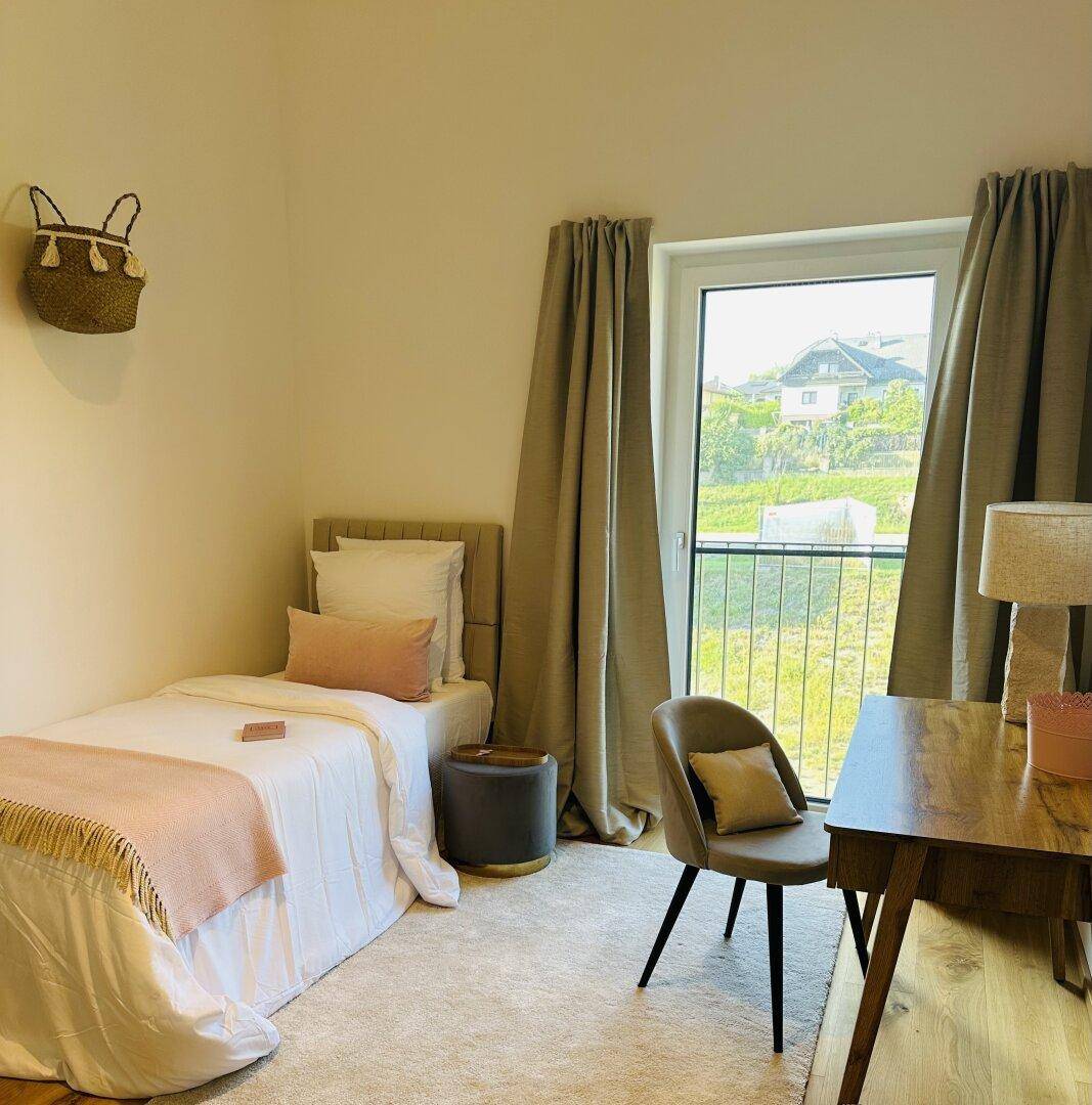 Helles Kinder- oder Gästezimmer mit Einzelbett, Schreibtisch und Fenster mit Blick ins Grüne.