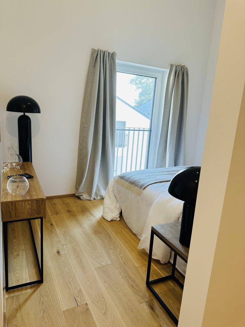 Schlafzimmer mit Holzboden, modernem Bett und Zugang zu einem französischen Balkon.