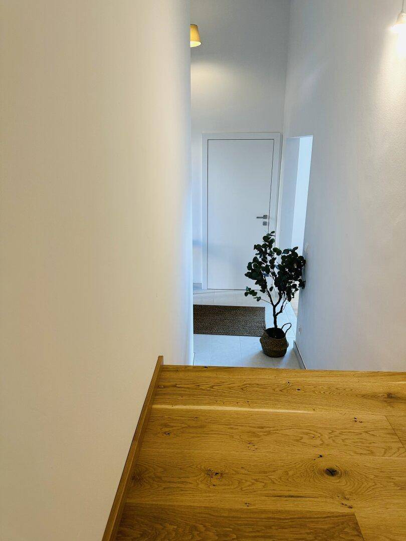Heller Flur mit Holztreppe und einer Tür am Ende des Ganges.
