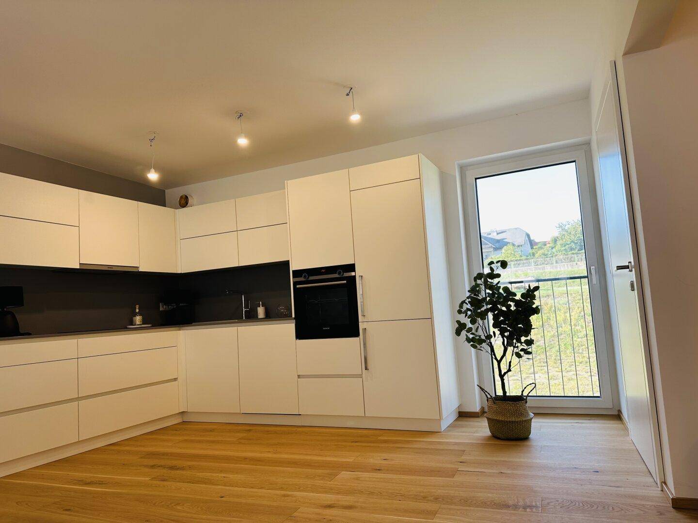 Moderne Einbauküche in Weiß mit integriertem Backofen und Fenster mit Blick ins Freie.