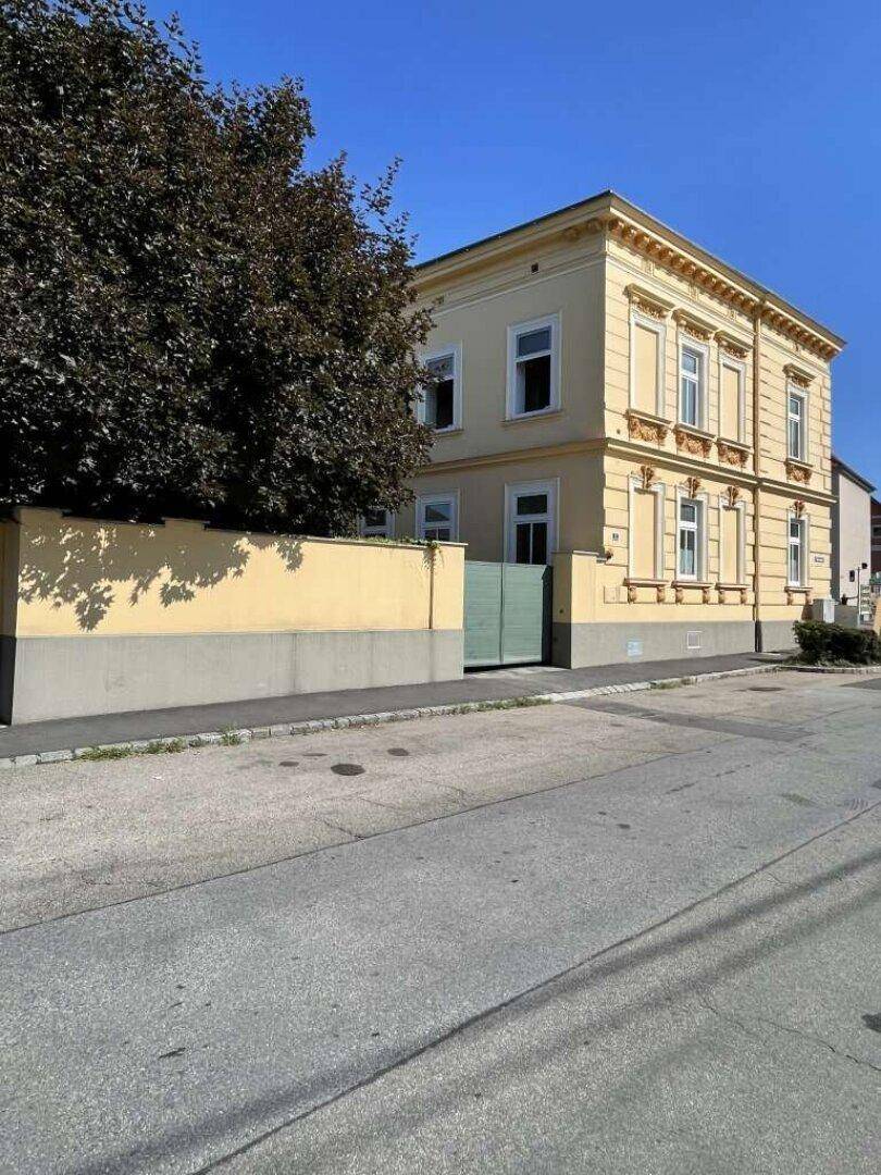 Historisches Gebäude mit gelber Fassade, weißen Fenstern und dekorativen Elementen an einem sonnigen Tag.