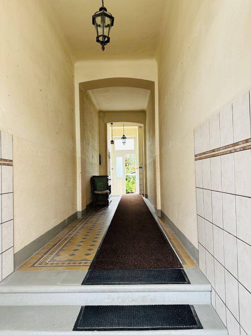 Langer Flur mit beigen Wänden, gemusterten Fliesen und traditioneller Beleuchtung.
