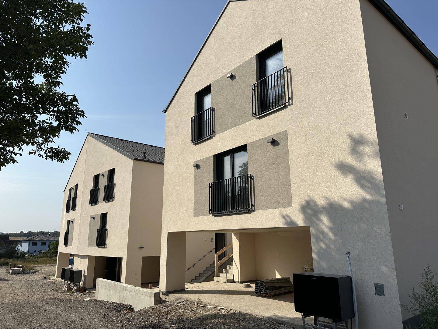 Zwei moderne Neubauten mit beiger Fassade, schwarzen Balkongeländern und Baustellenbereich.