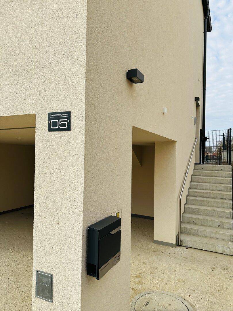 Eingangsbereich eines modernen Gebäudes mit Hausnummer, Briefkasten und Außentreppe.
