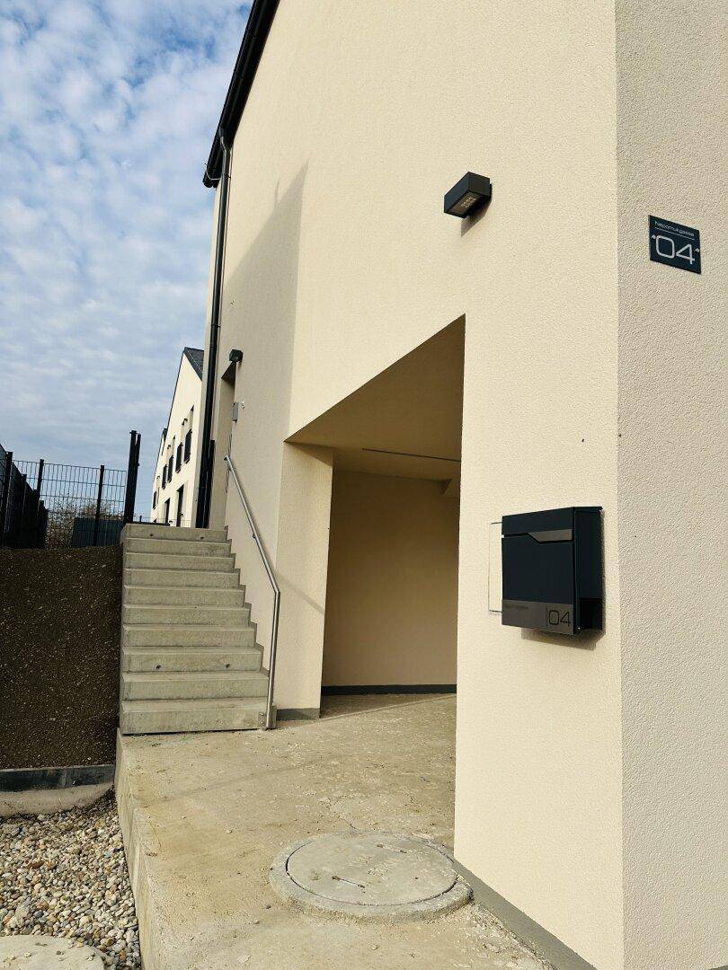 Eingangsbereich eines Neubaus mit Treppe, Briefkasten und moderner Außenbeleuchtung.