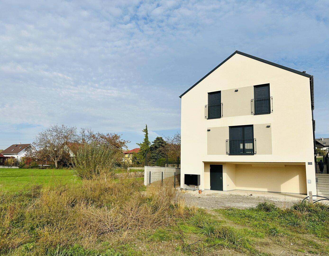Neubau-Einfamilienhaus mit heller Fassade, Satteldach und französischen Balkonen in ländlicher Umgebung.