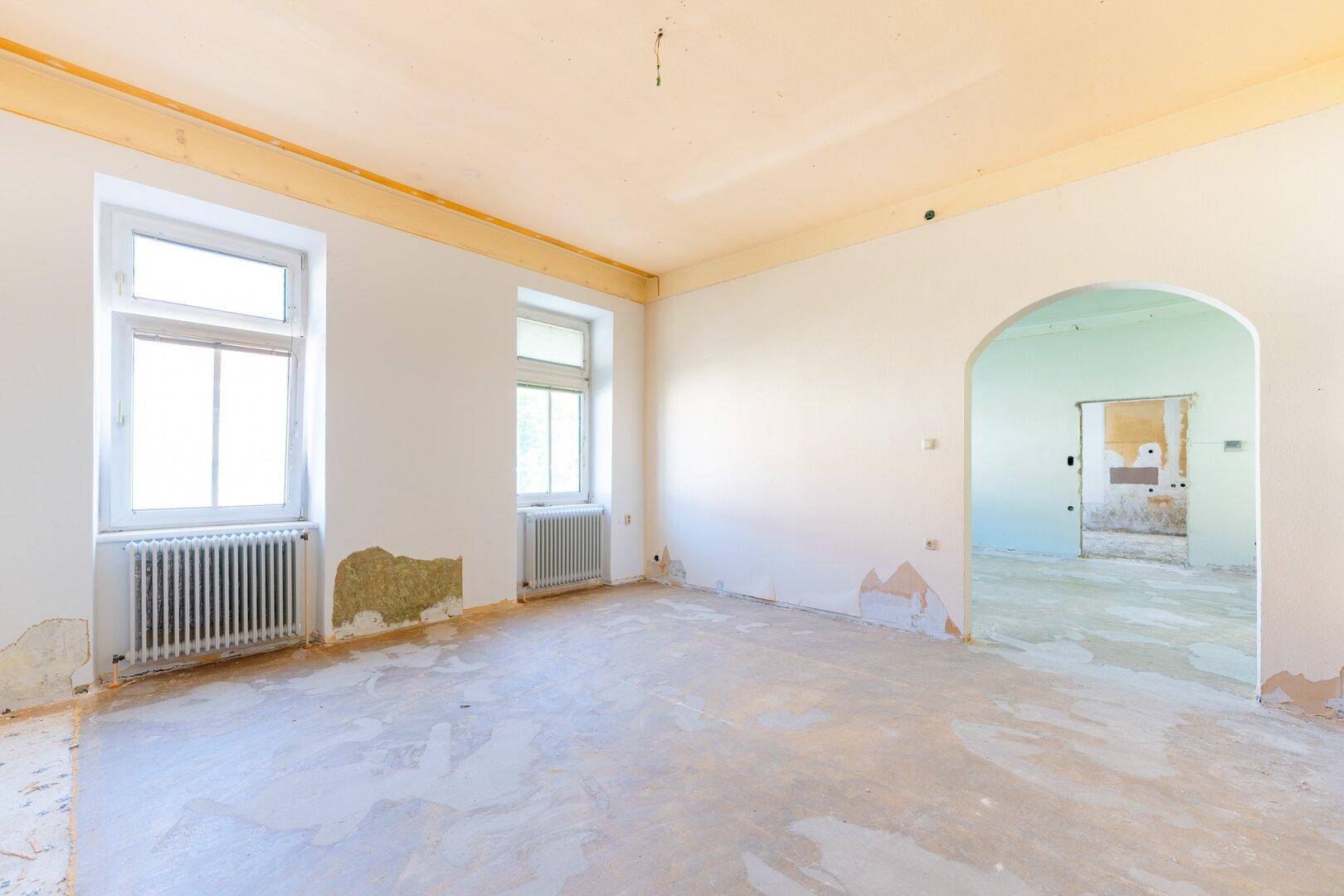 Leerer Raum in Renovierung mit abblätternder Farbe und Blick auf einen weiteren Raum.