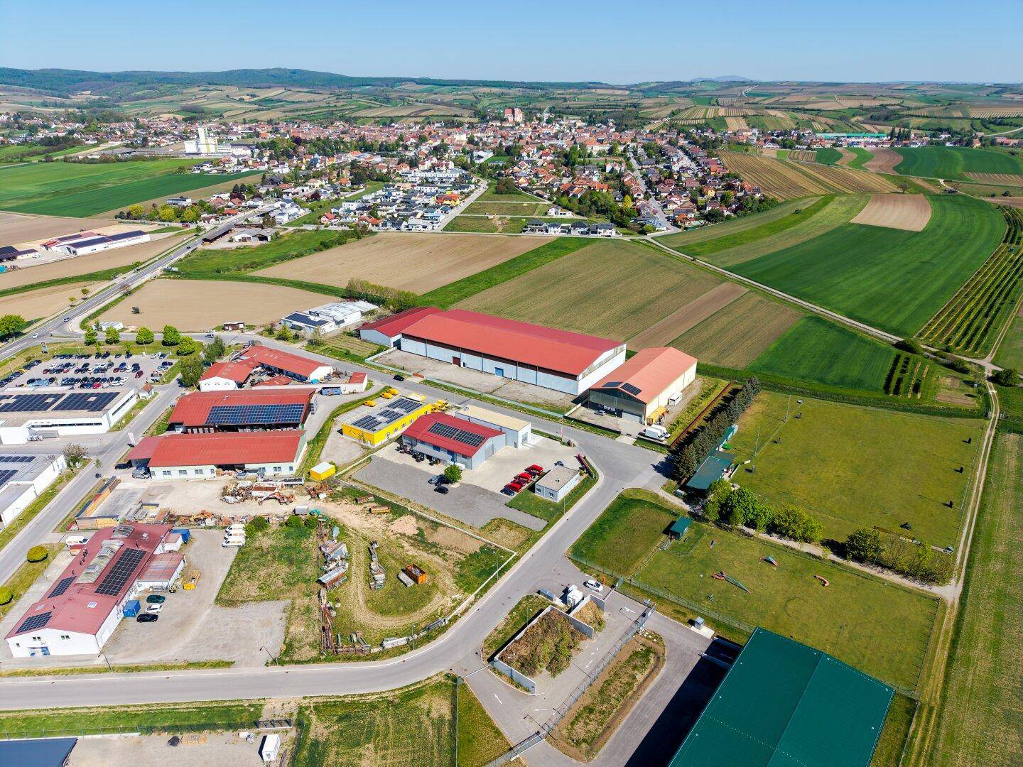 Panoramische Luftaufnahme eines Gewerbegebiets am Rande einer Kleinstadt, umgeben von Feldern und Natur.