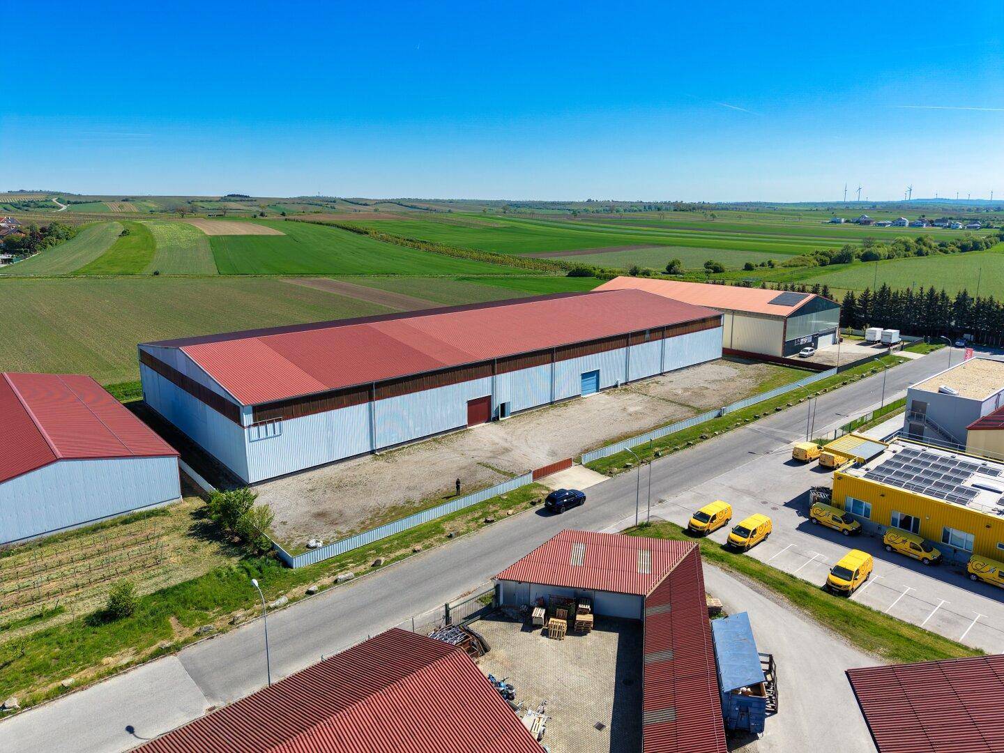 Weitläufige Luftaufnahme eines Gewerbegebiets mit mehreren Hallen und angrenzenden landwirtschaftlichen Flächen.