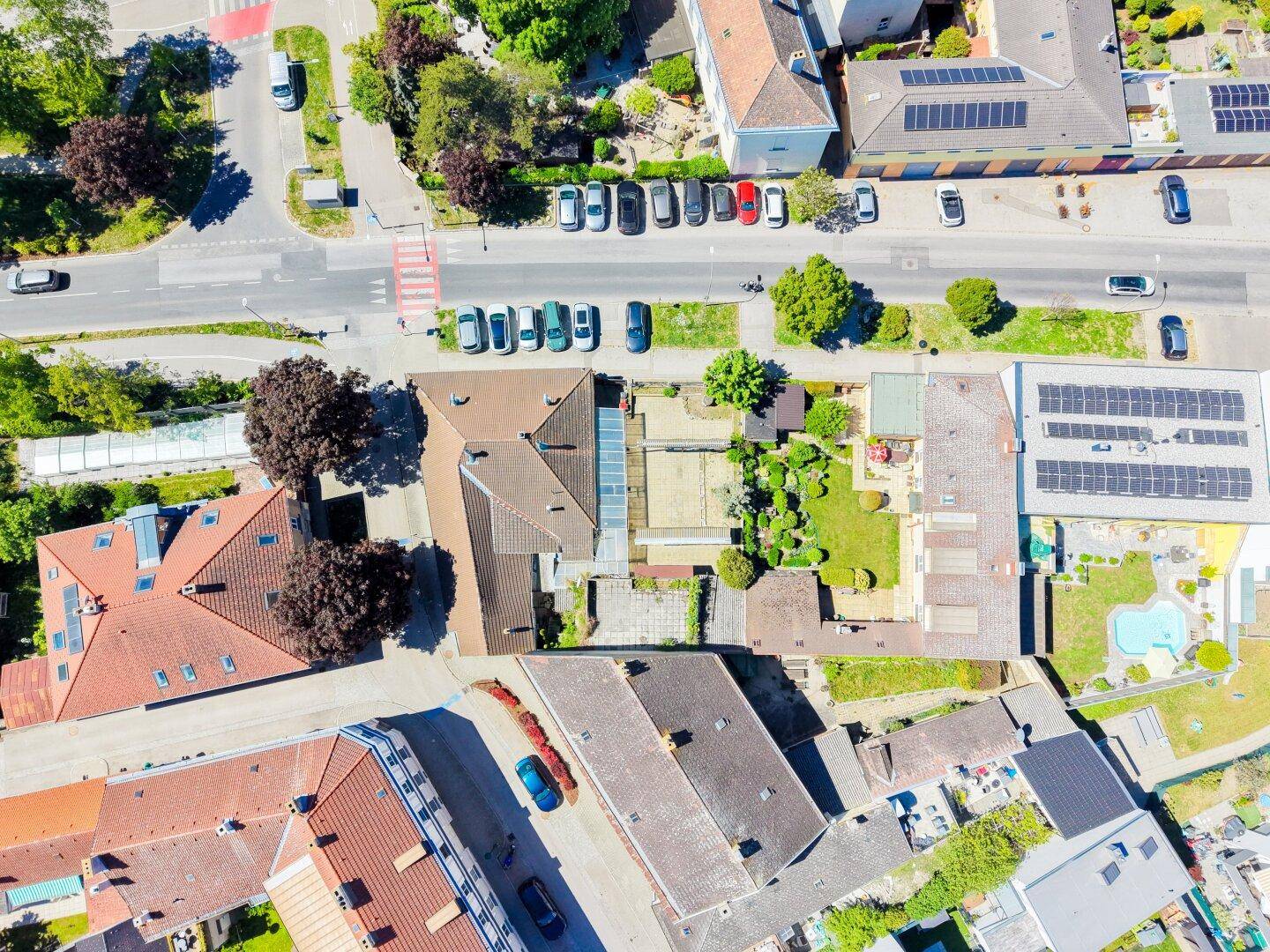 Draufsicht auf ein Wohngebiet mit Dächern, Straßen, parkenden Autos und einem Pool im Garten.
