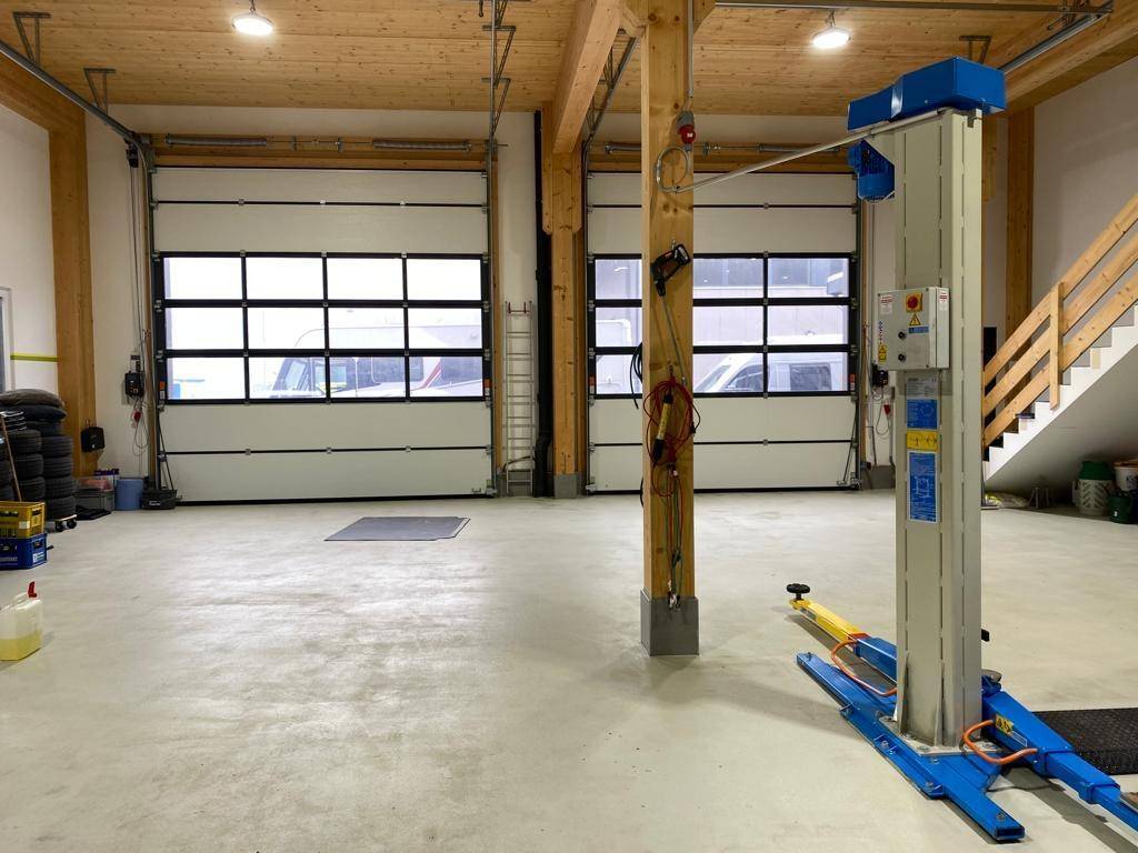 Geräumige Werkstatt mit zwei großen Sektionaltoren, Fahrzeuglift und Holzkonstruktion.