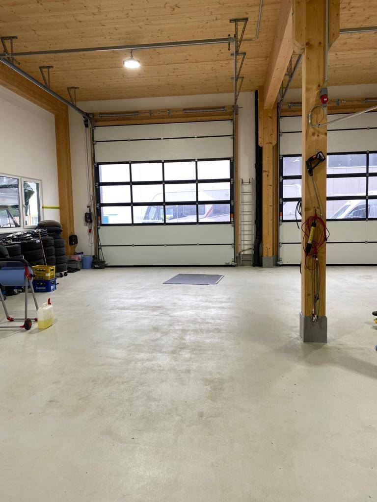 Heller Werkstattbereich mit Sektionaltoren, Holzbalken und einem Fahrzeuglift, gut ausgestattet.
