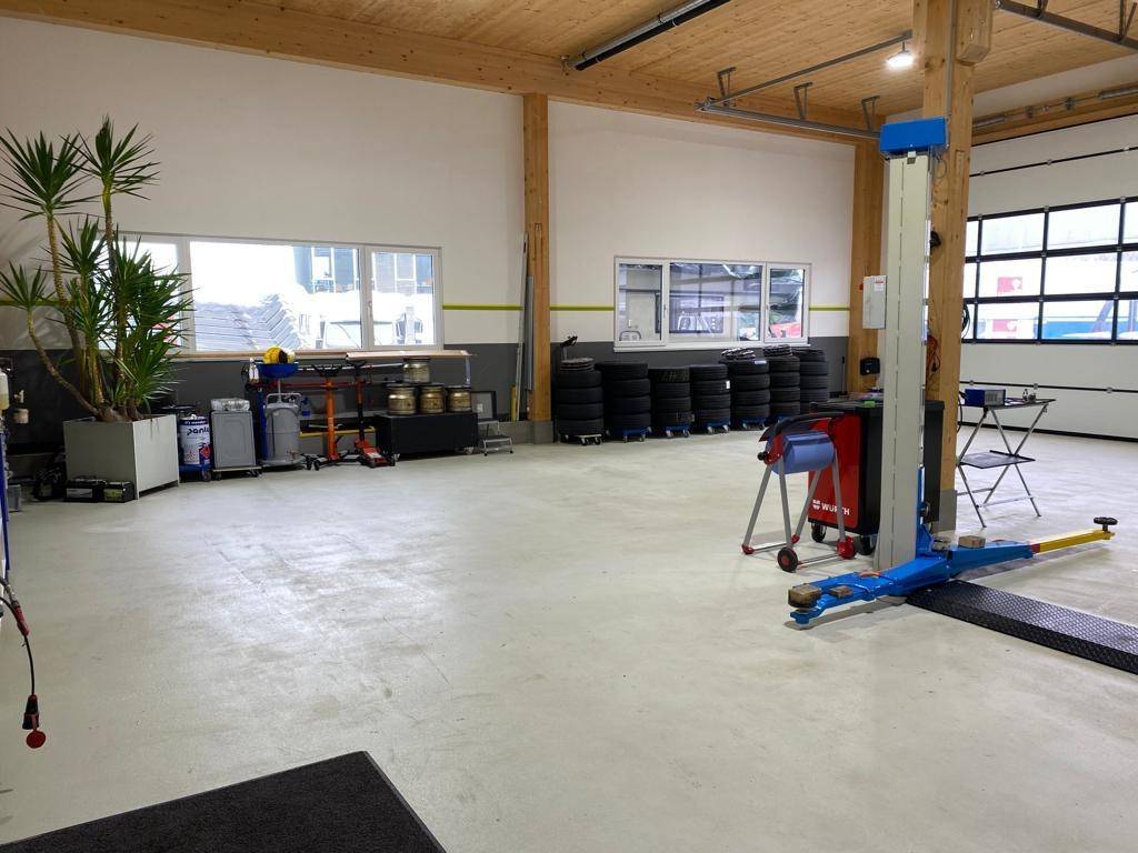 Werkstatt mit Fahrzeuglift, Reifenlager und großen Fenstern, bietet viel Platz und Licht.