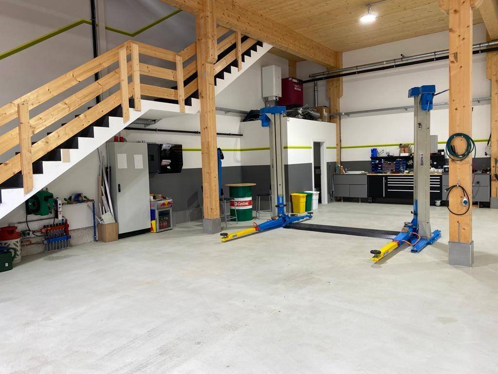 Helle Werkstatt mit sichtbaren Holzbalken, Betonboden und einem professionellen Fahrzeuglift.