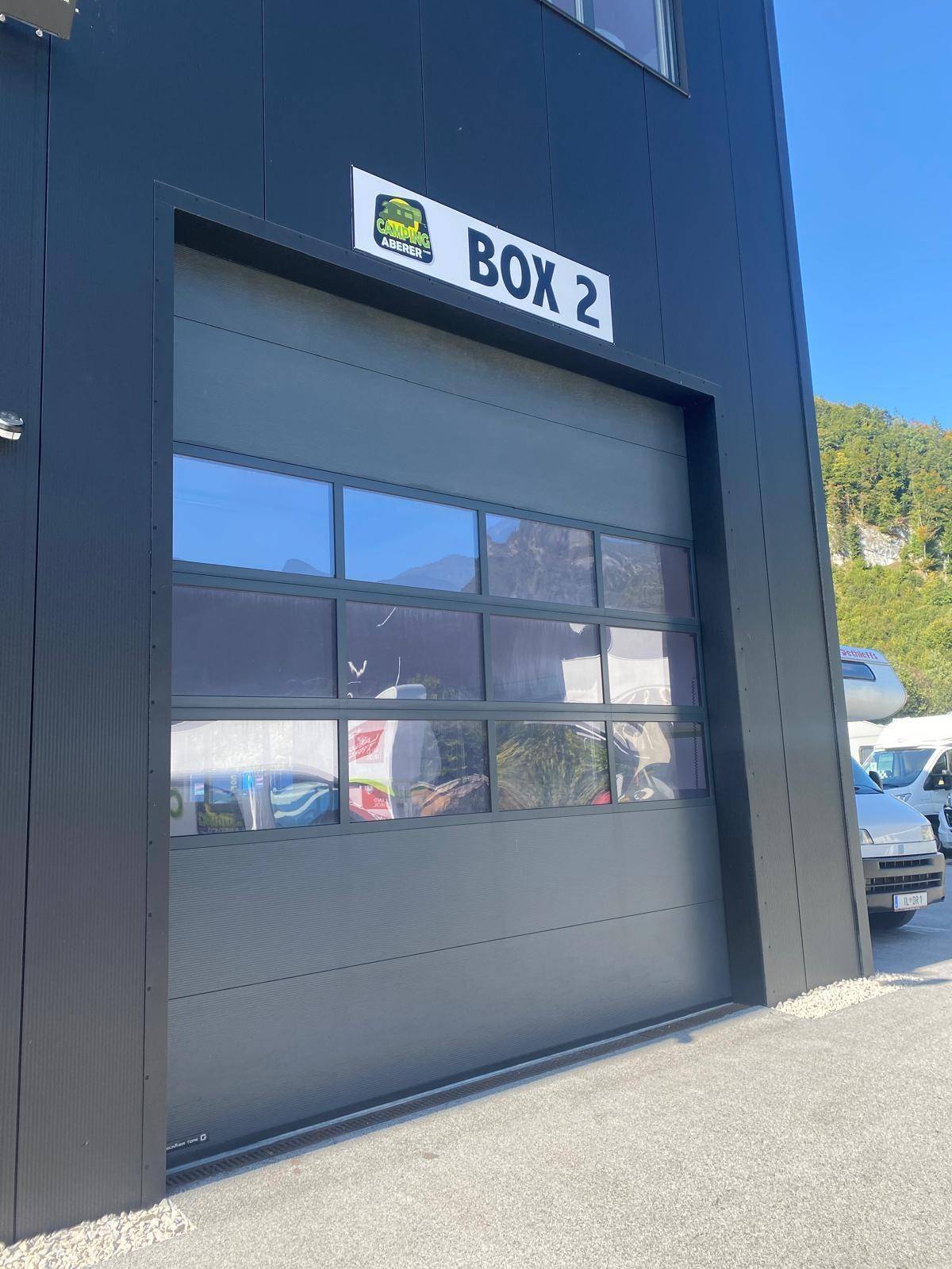 Moderne schwarze Garagentore mit Fenstern und Beschriftung "BOX 2" an der Fassade.