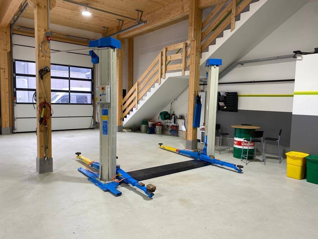 Werkstattbereich mit großem Garagentor, Fahrzeuglift und Holztreppe, ideal für Fahrzeugwartung.