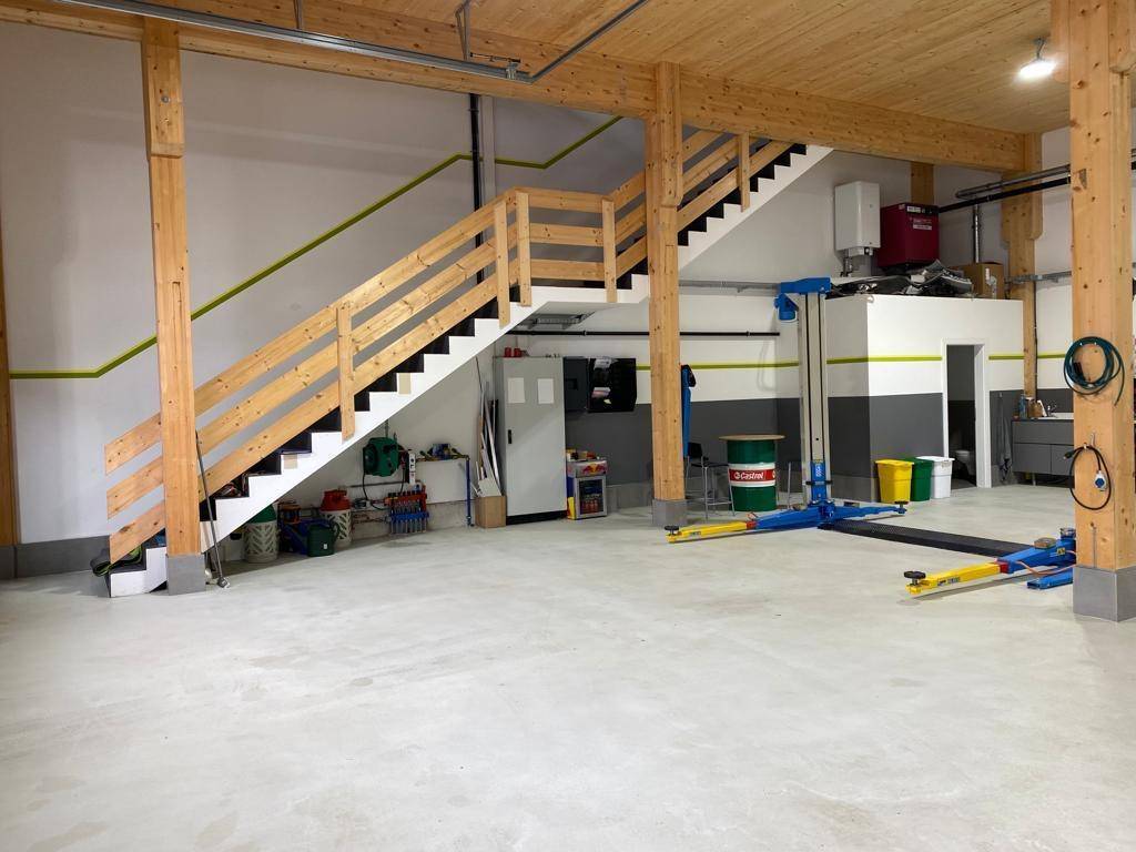 Saubere Werkstatt mit Holztreppe, Fahrzeuglift und Betonboden, bereit für den Einsatz.