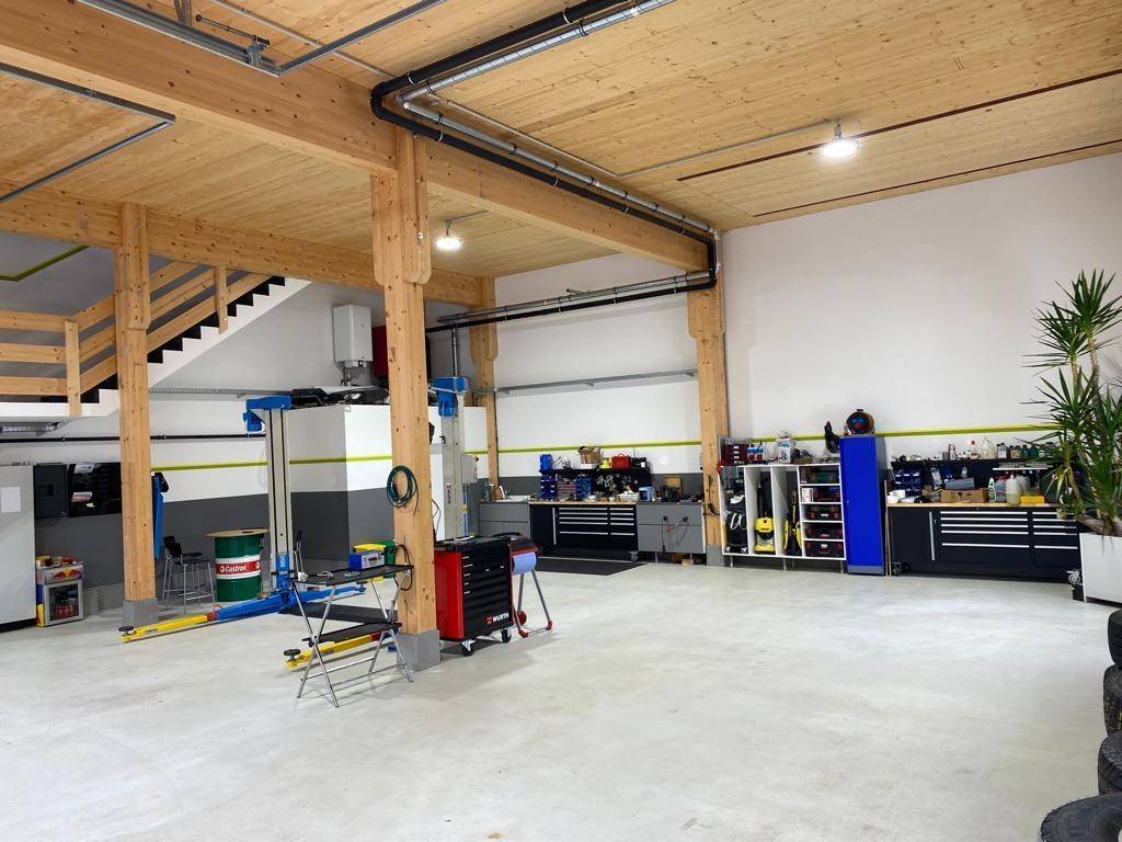 Geräumige Werkstatt mit Holzbalken, Betonboden und umfangreichen Arbeitsbereichen, gut beleuchtet.