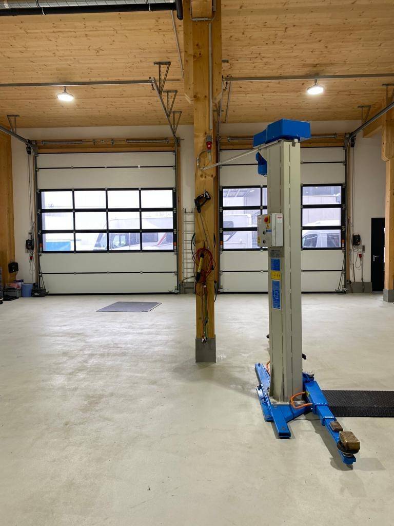 Großer Werkstattraum mit zwei Sektionaltoren und einem Fahrzeuglift, viel Tageslicht.