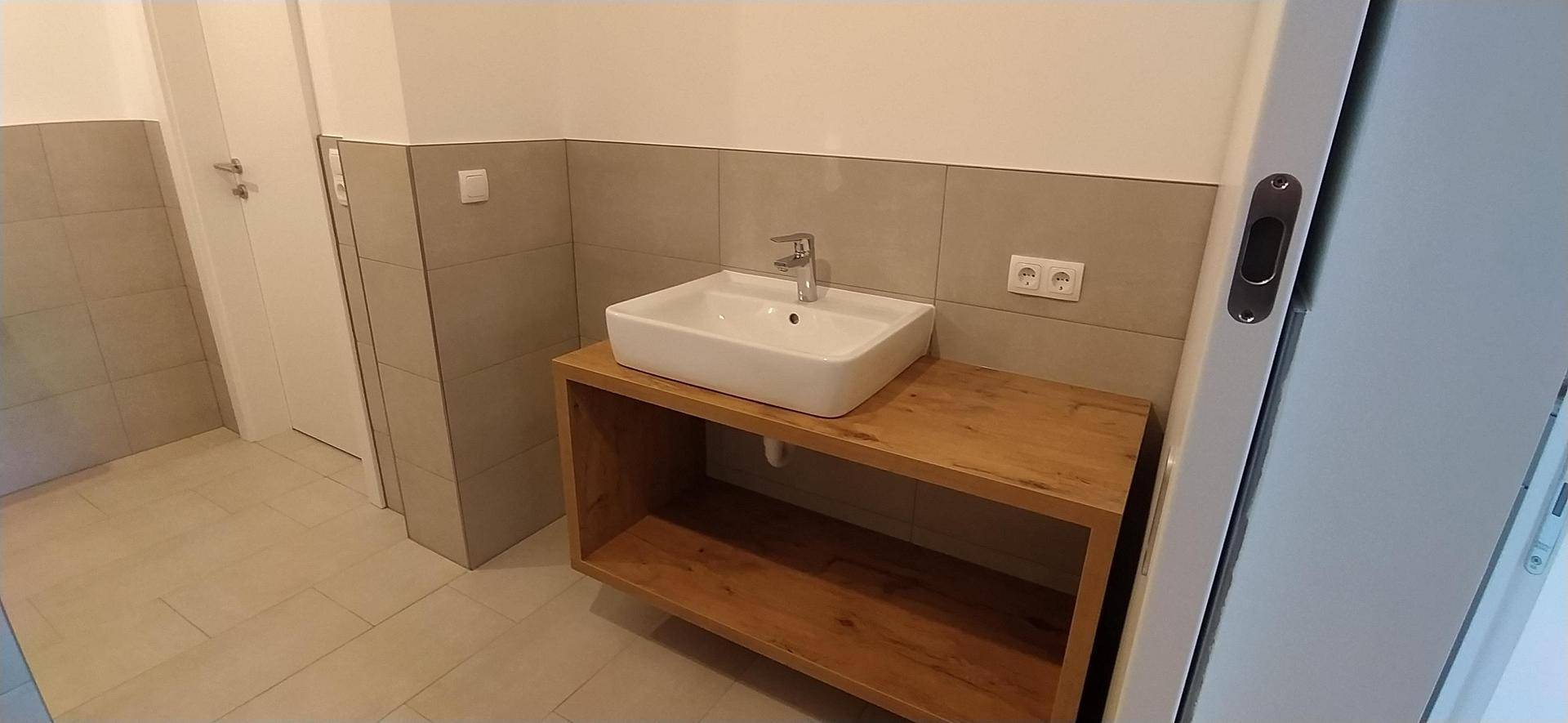 Modernes Badezimmer mit Einzelwaschbecken auf Holzunterschrank und grauen Fliesen.