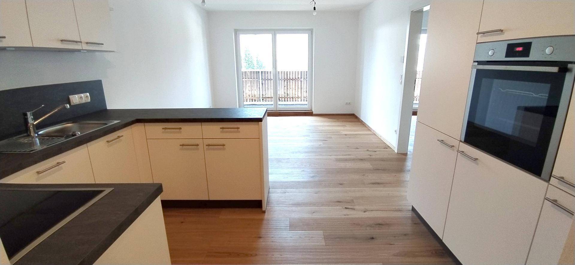 Funktionale Küche mit weißen Schränken, Spüle und Kochfeld, mit Blick auf den Balkon.