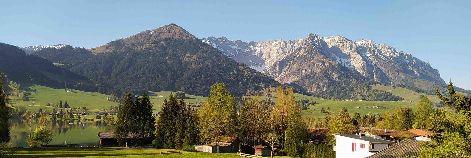 Malerischer Blick auf Berge, See und grüne Landschaft mit vereinzelten Häusern.