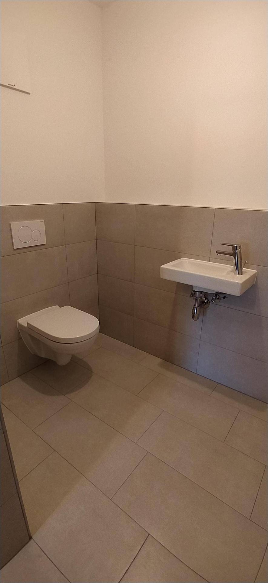 Gäste-WC mit wandhängender Toilette und kleinem Waschbecken, modern gefliest.