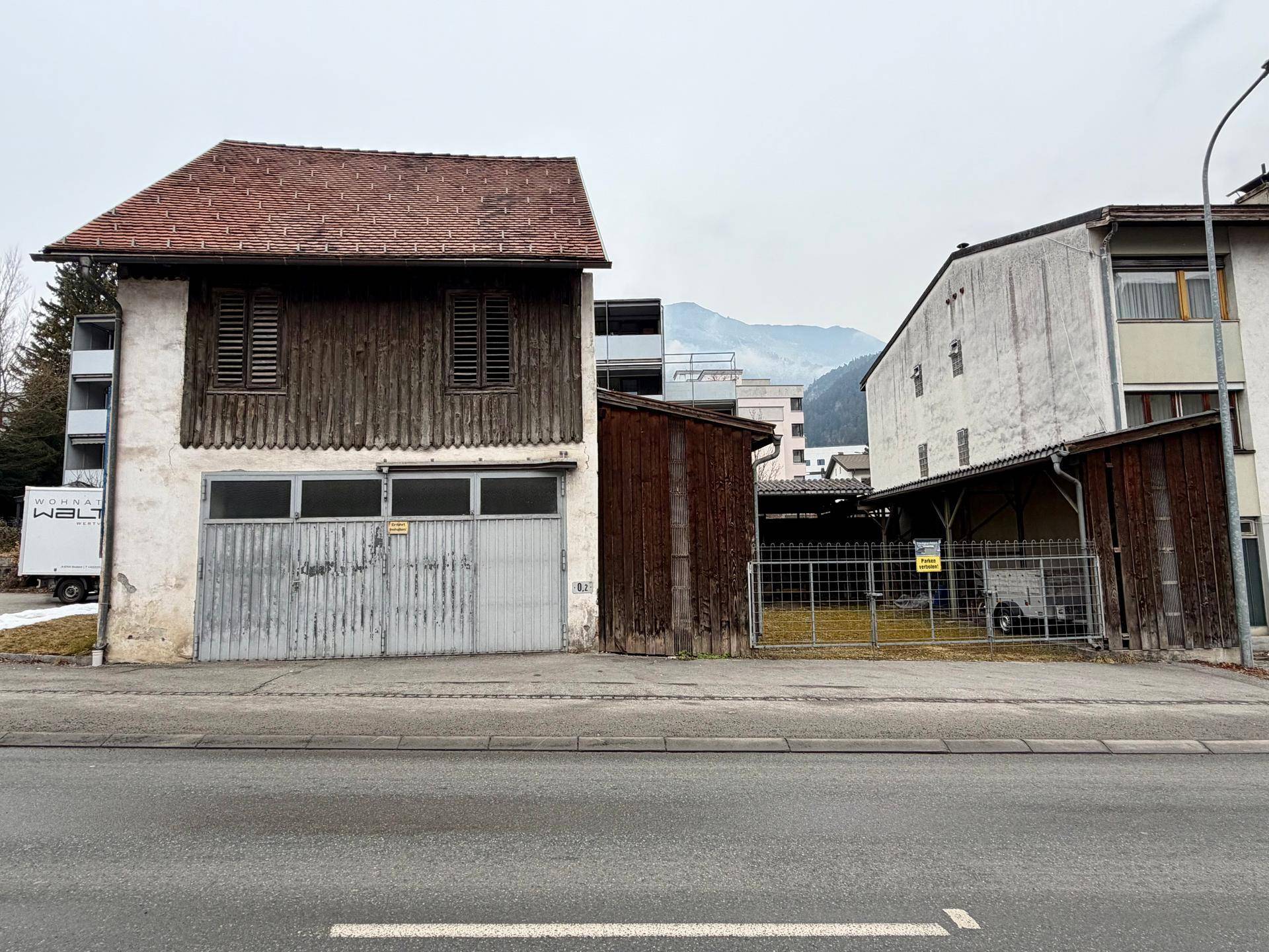Ansicht des alten Gebäudes von der Straße aus mit Holzelementen, Garagentoren und einem Ziegeldach.
