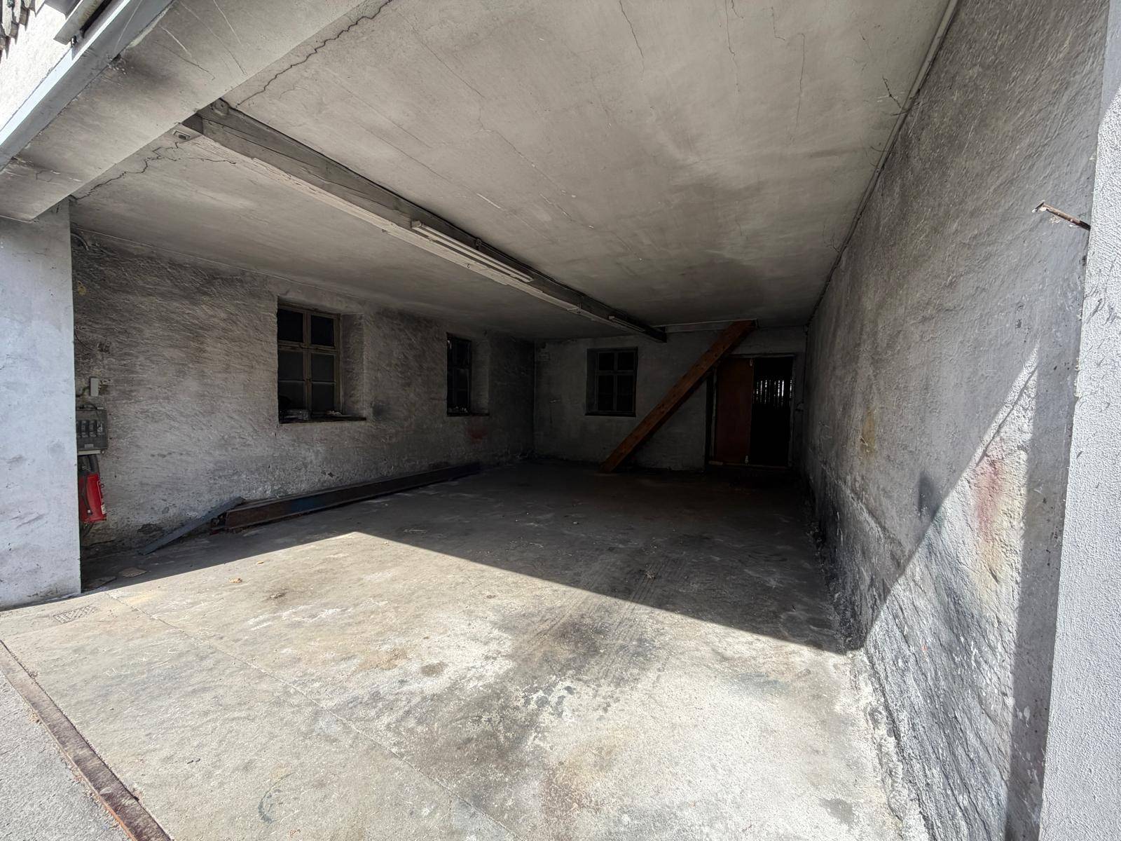 Leerer Garagenraum mit rauen Betonwänden und -boden, ausgestattet mit kleinen Fenstern.