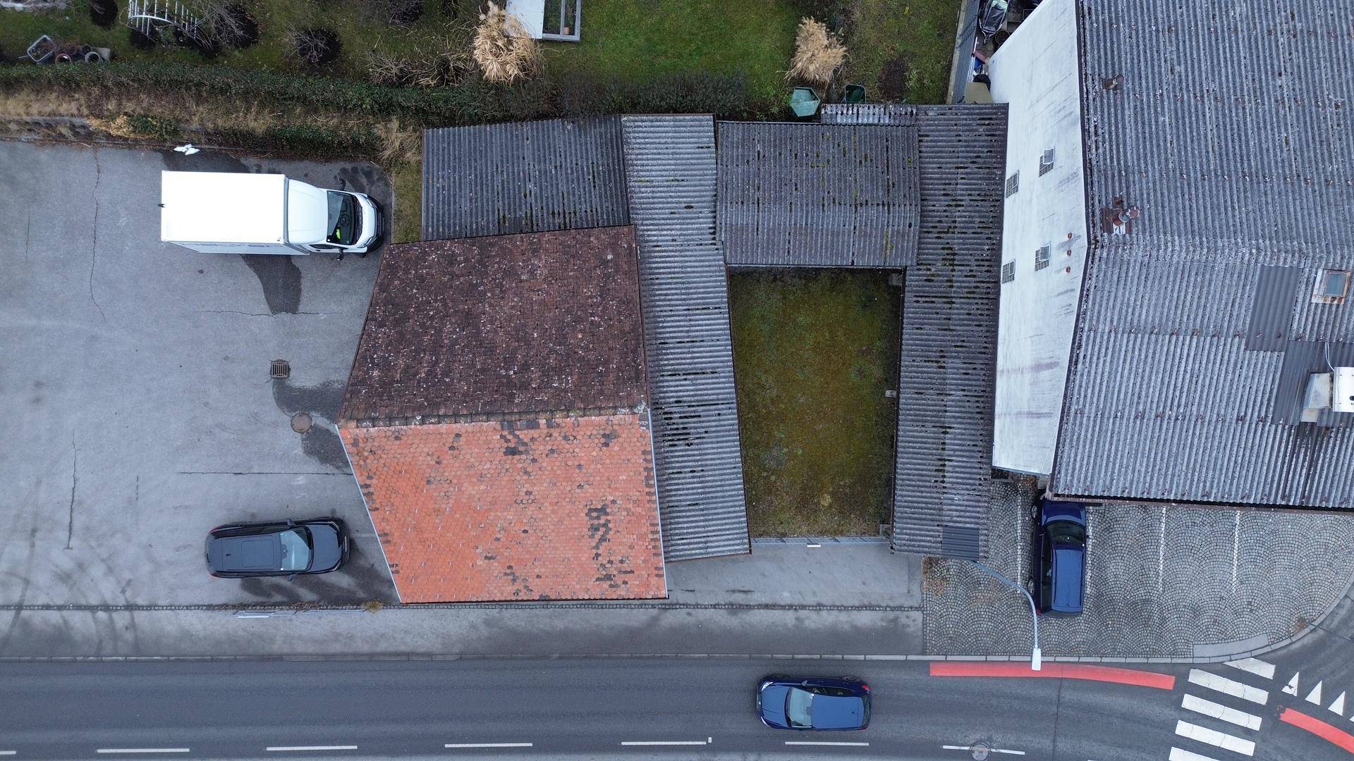 Draufsicht auf das Grundstück mit einem alten Haus, einem Innenhof und angrenzenden Parkplätzen und Straßen.