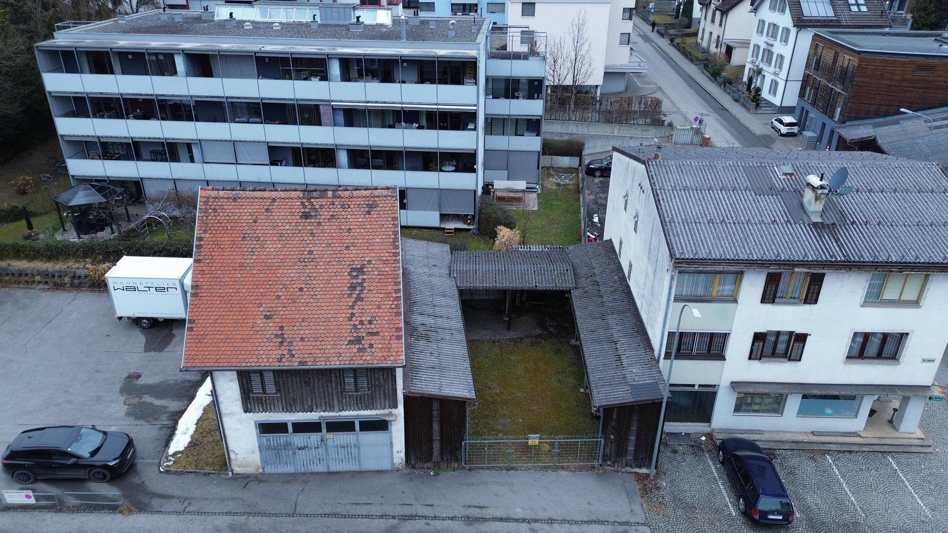 Luftaufnahme eines alten Gebäudes mit Ziegeldach und angrenzendem Hofbereich, umgeben von weiteren Gebäuden.