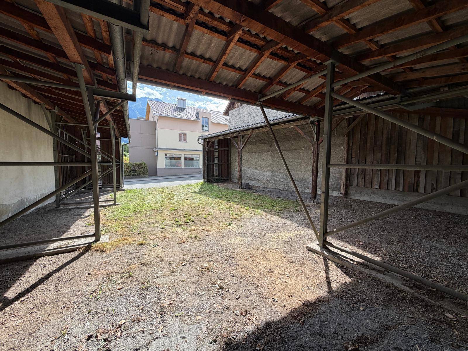 Überdachter Außenbereich mit Erdboden und Holzkonstruktion, Blick auf die Straße und umliegende Gebäude.