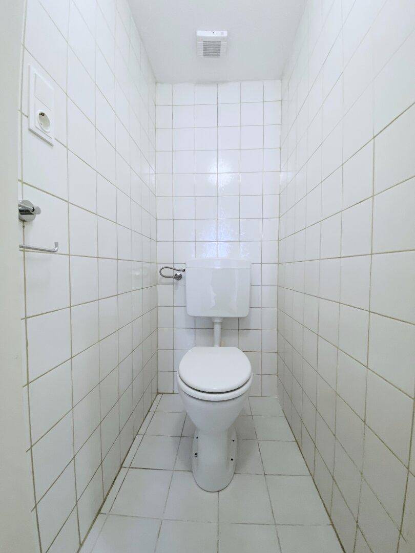 Kleines separates WC mit weißen Fliesen an Wänden und Boden.