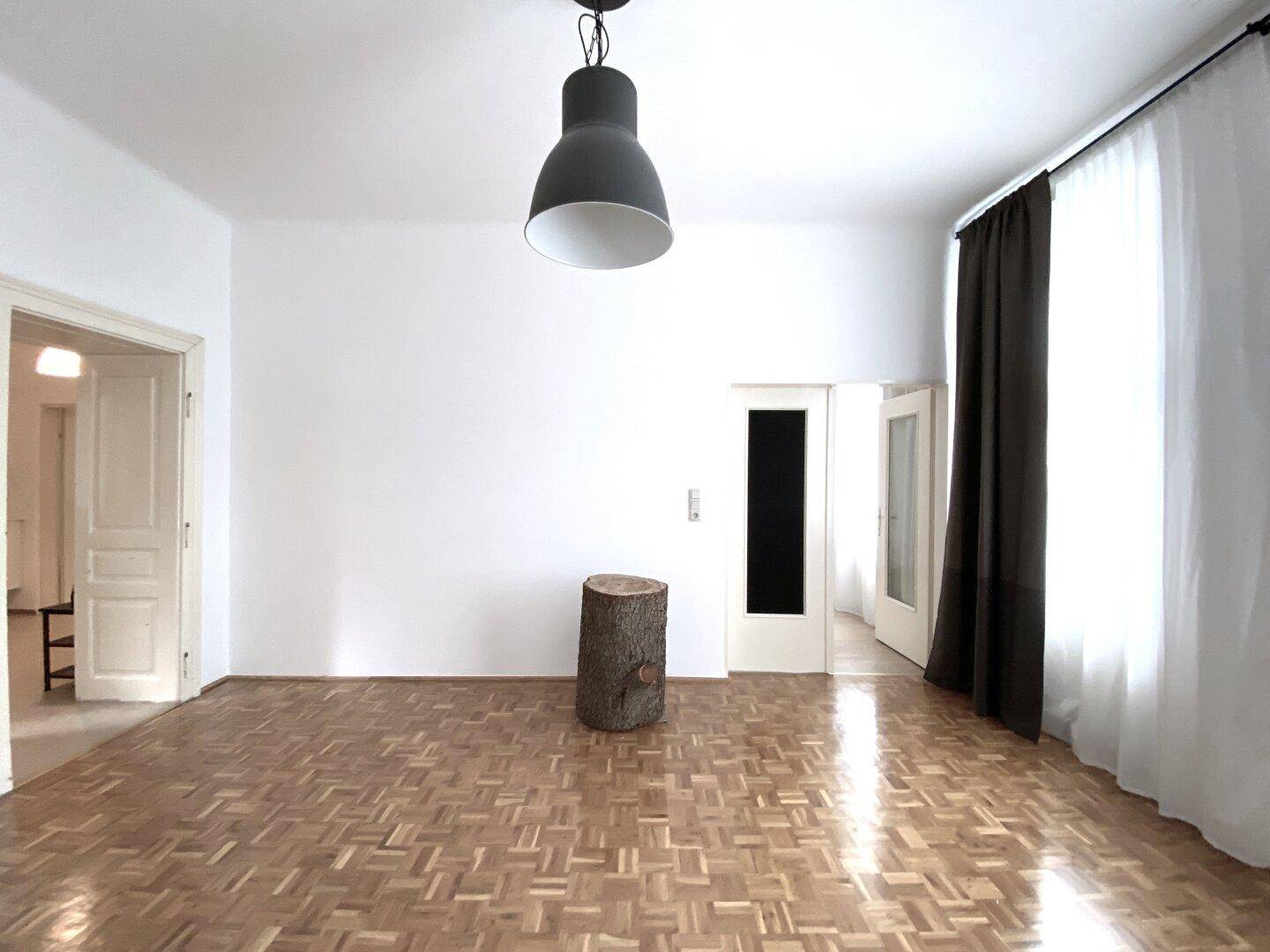 Geräumiges Wohnzimmer mit klassischem Parkettboden und Zugang zu weiteren Räumen.