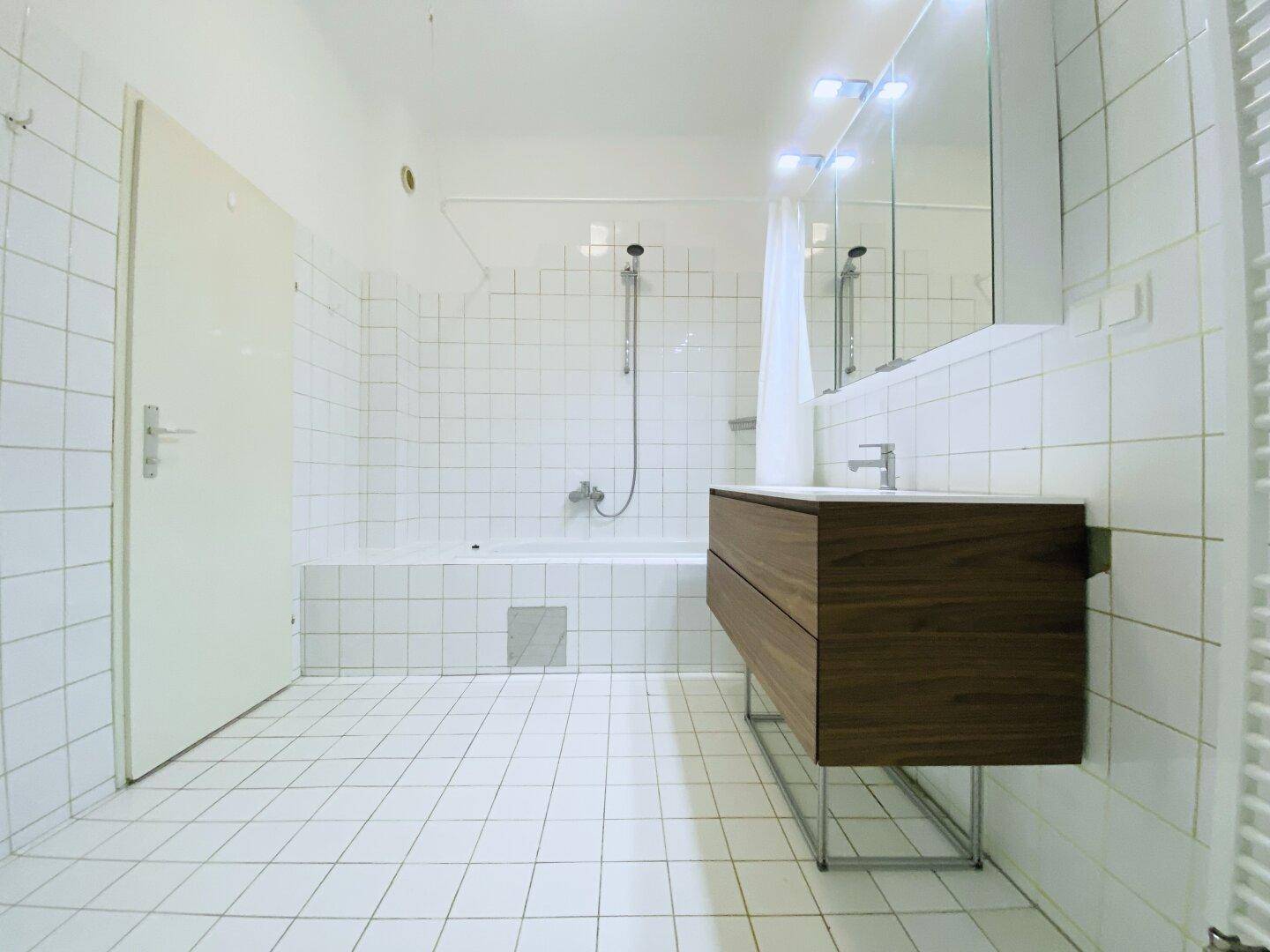 Badezimmer mit Badewanne, weißen Wandfliesen und einem eleganten Holzwaschtisch.
