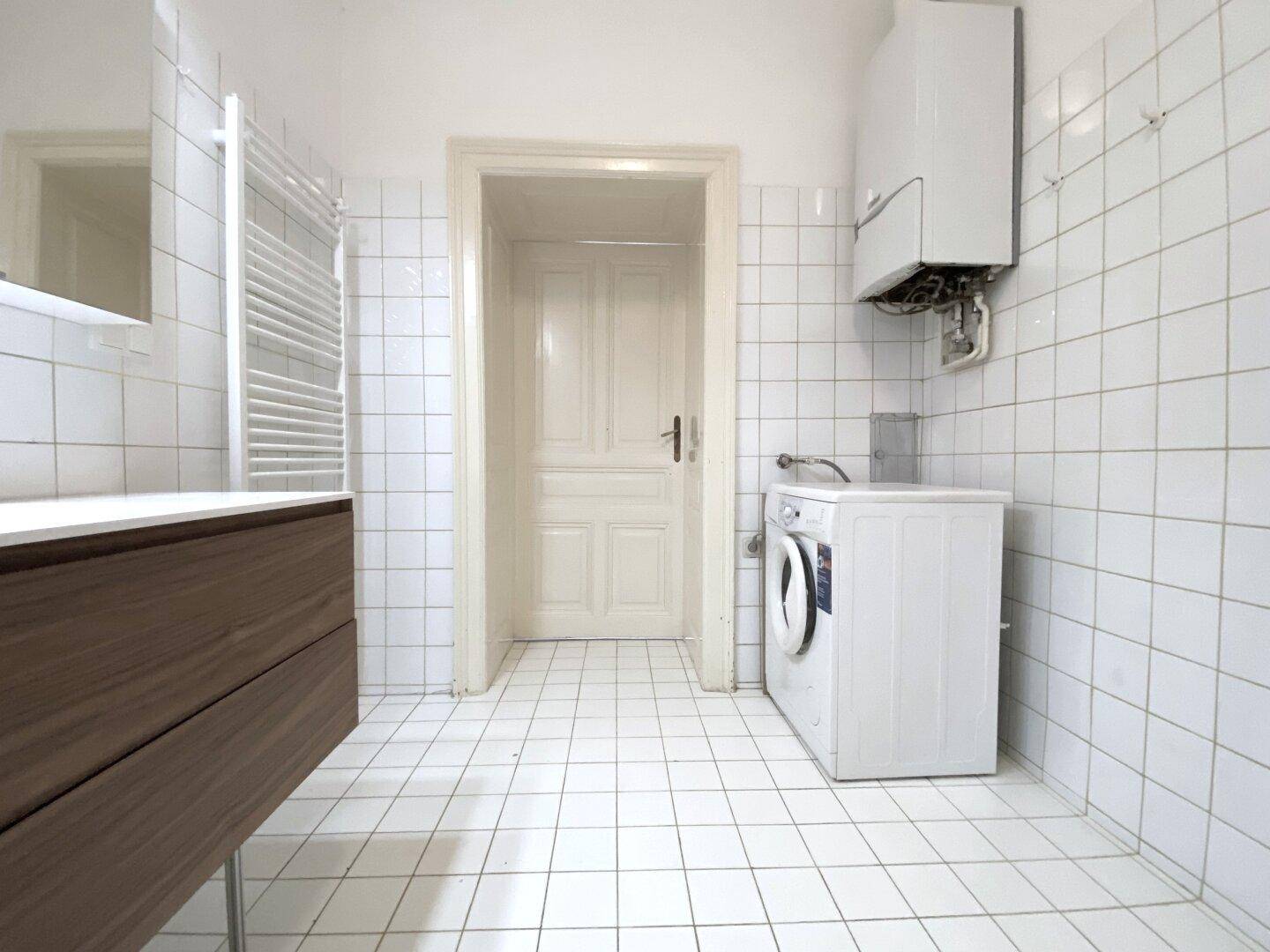 Badezimmer mit weißen Fliesen, Waschmaschine und einem modernen Holzwaschtisch.
