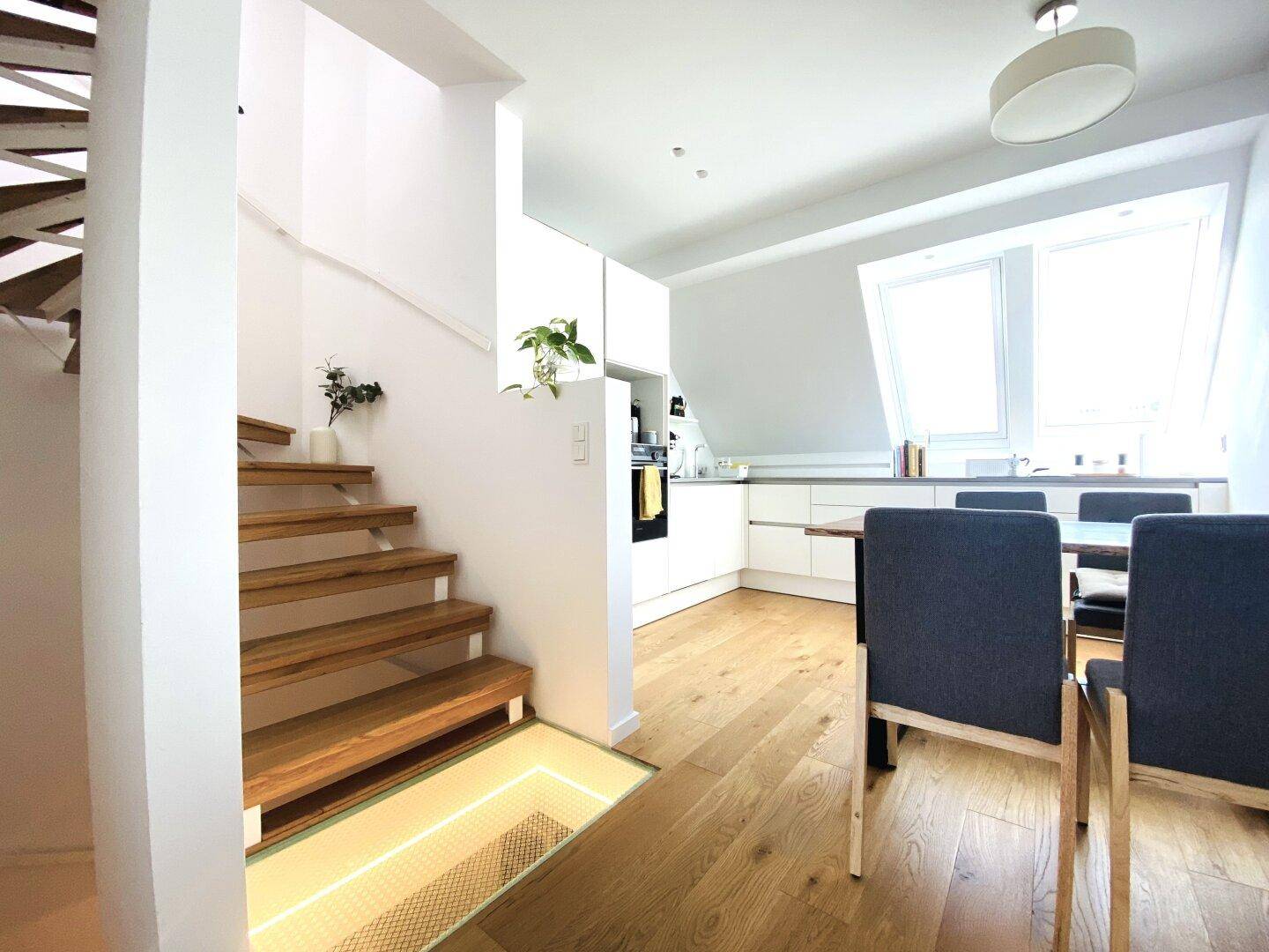 Heller offener Wohnbereich mit Holztreppe, moderner Küche und Essbereich.