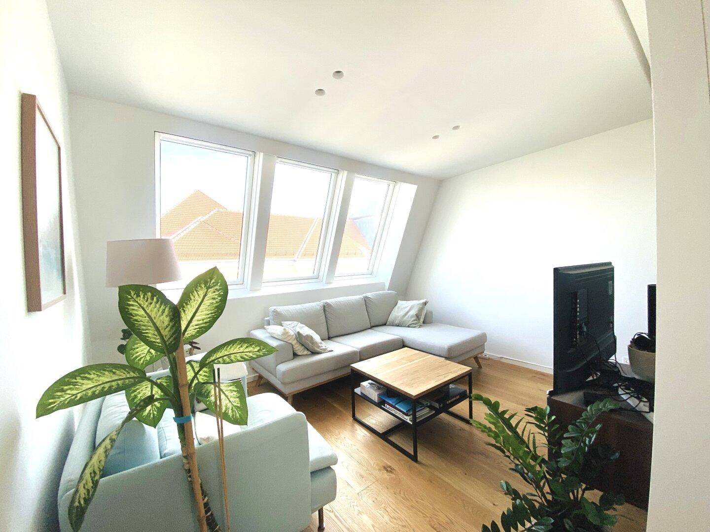 Gemütliches Wohnzimmer mit Dachschrägen, großen Fenstern und hellem Holzfußboden.