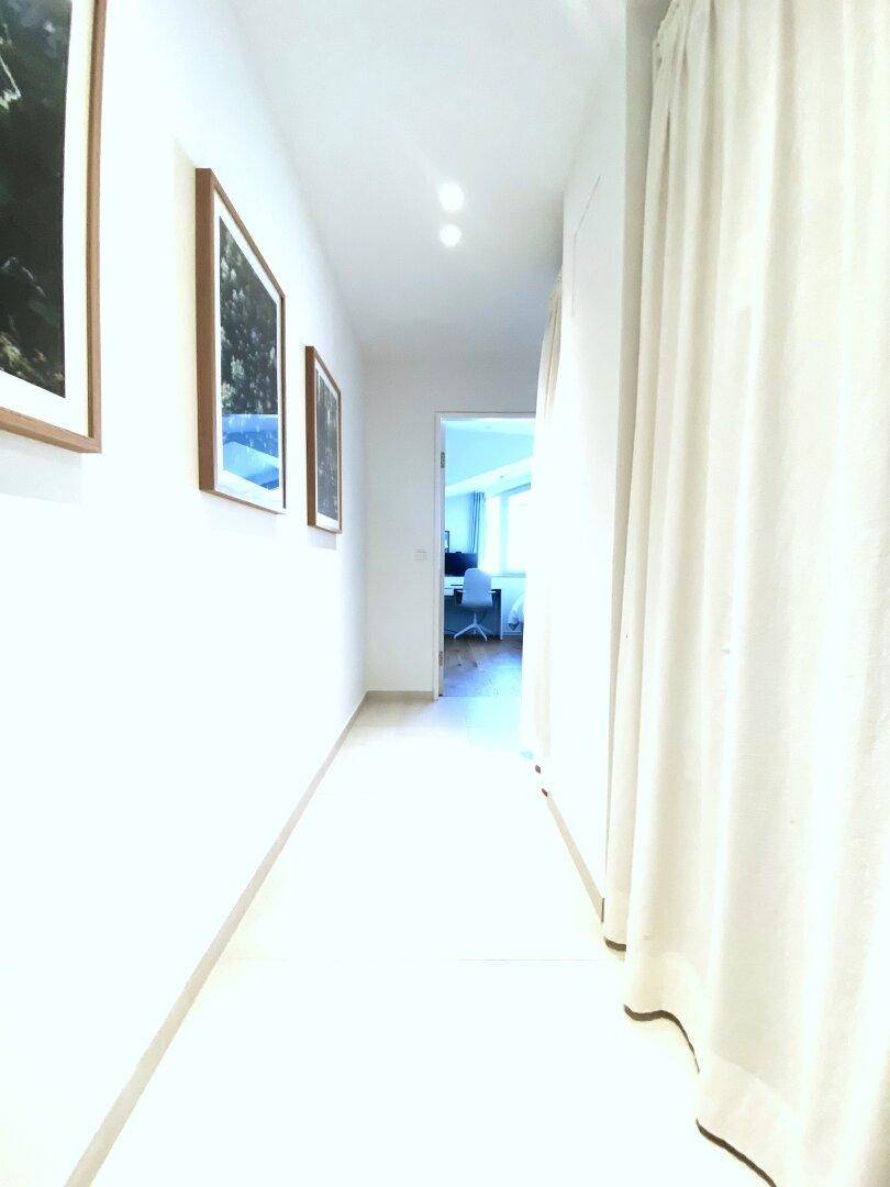 Langer, heller Flur mit Bildern an der Wand und Vorhängen.