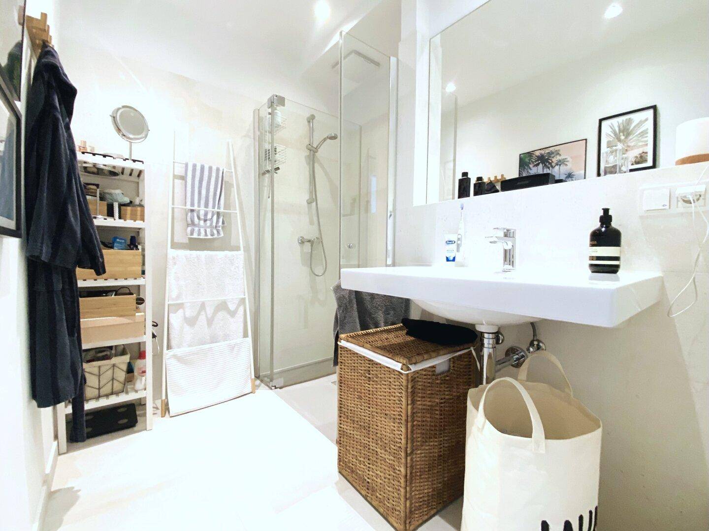 Modernes Badezimmer mit ebenerdiger Dusche, weißem Waschtisch und viel Stauraum.