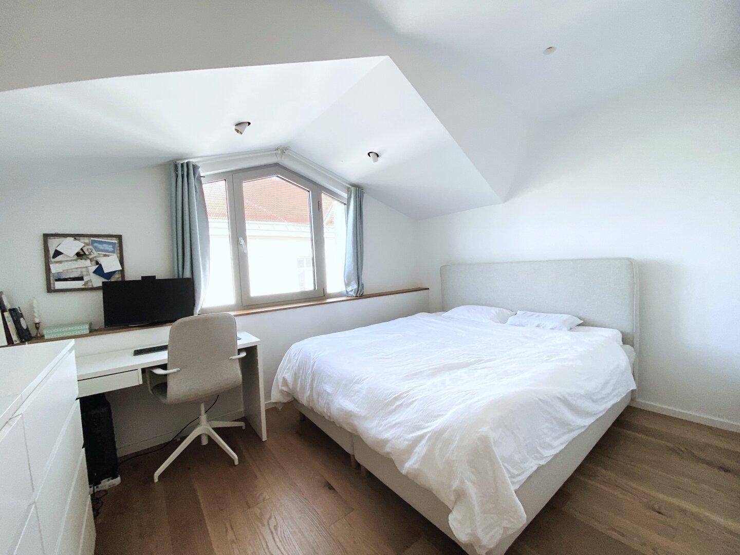 Helles Schlafzimmer mit Holzboden, Schreibtisch und Dachschrägenfenstern.