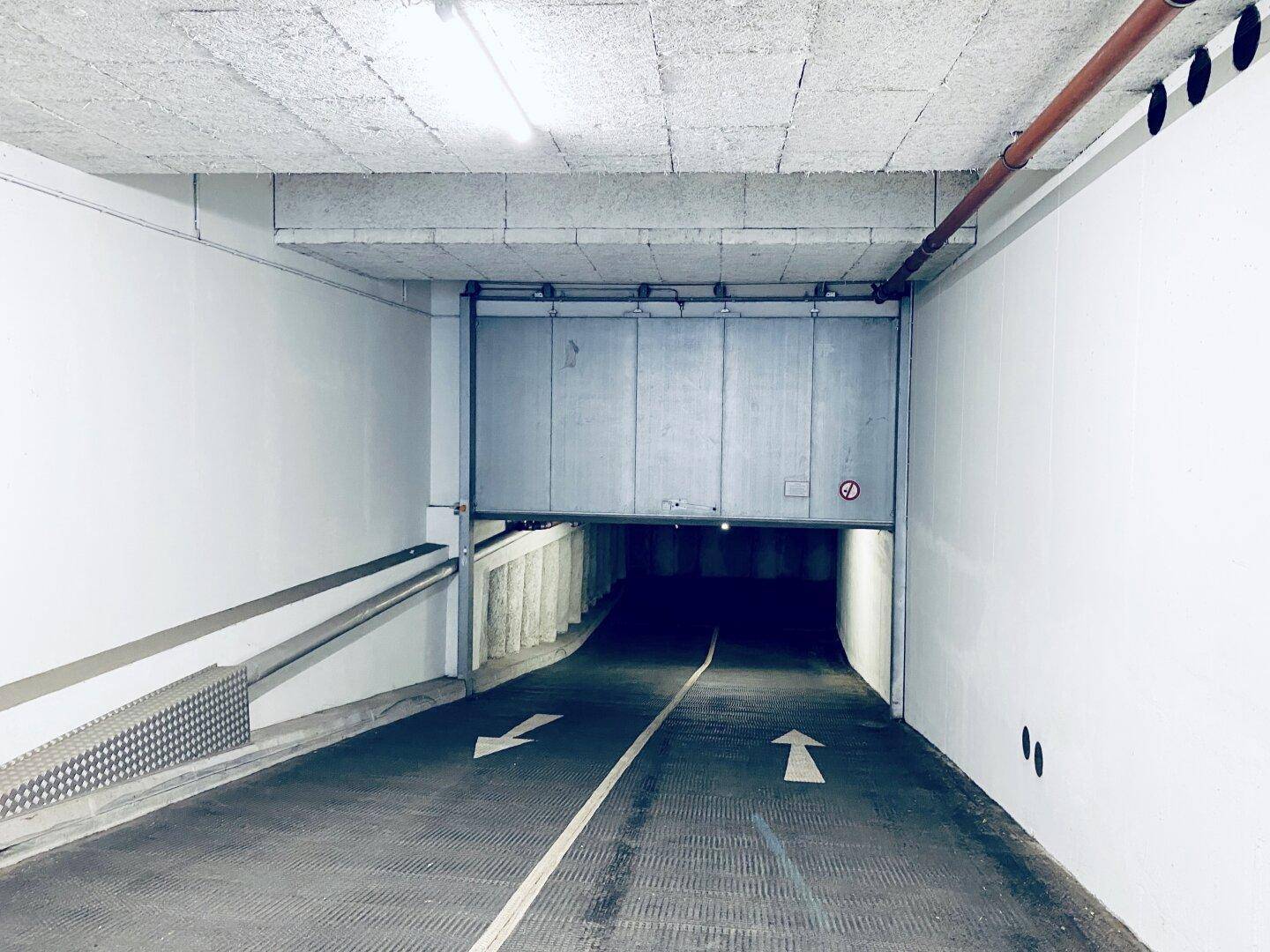Einfahrt zu einer Tiefgarage mit Rampe und einem großen Rolltor, das den Zugang sichert.