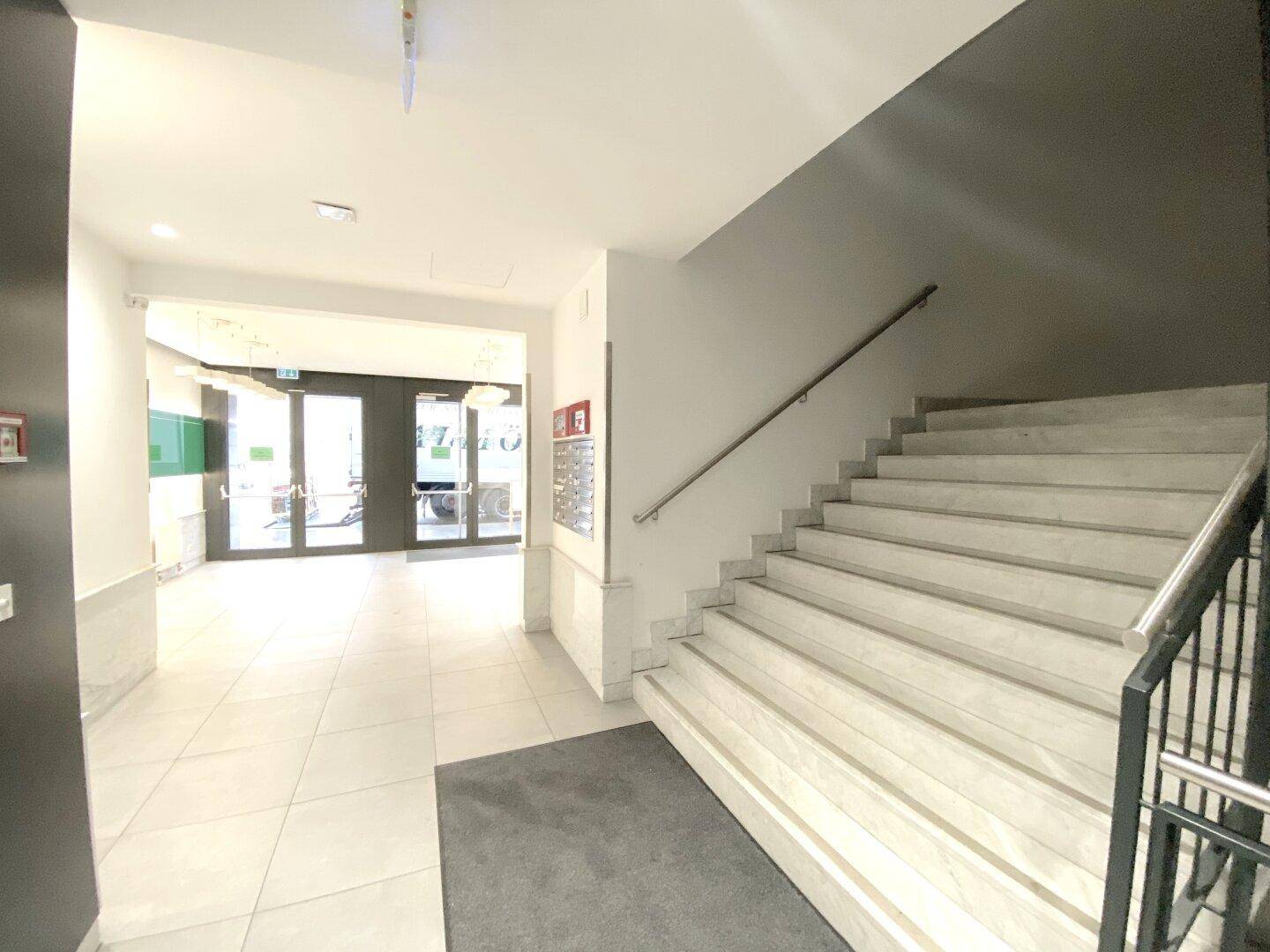 Geräumiger Eingangsbereich mit eleganter Marmortreppe und hellem Fliesenboden, der zu den oberen Etagen führt.