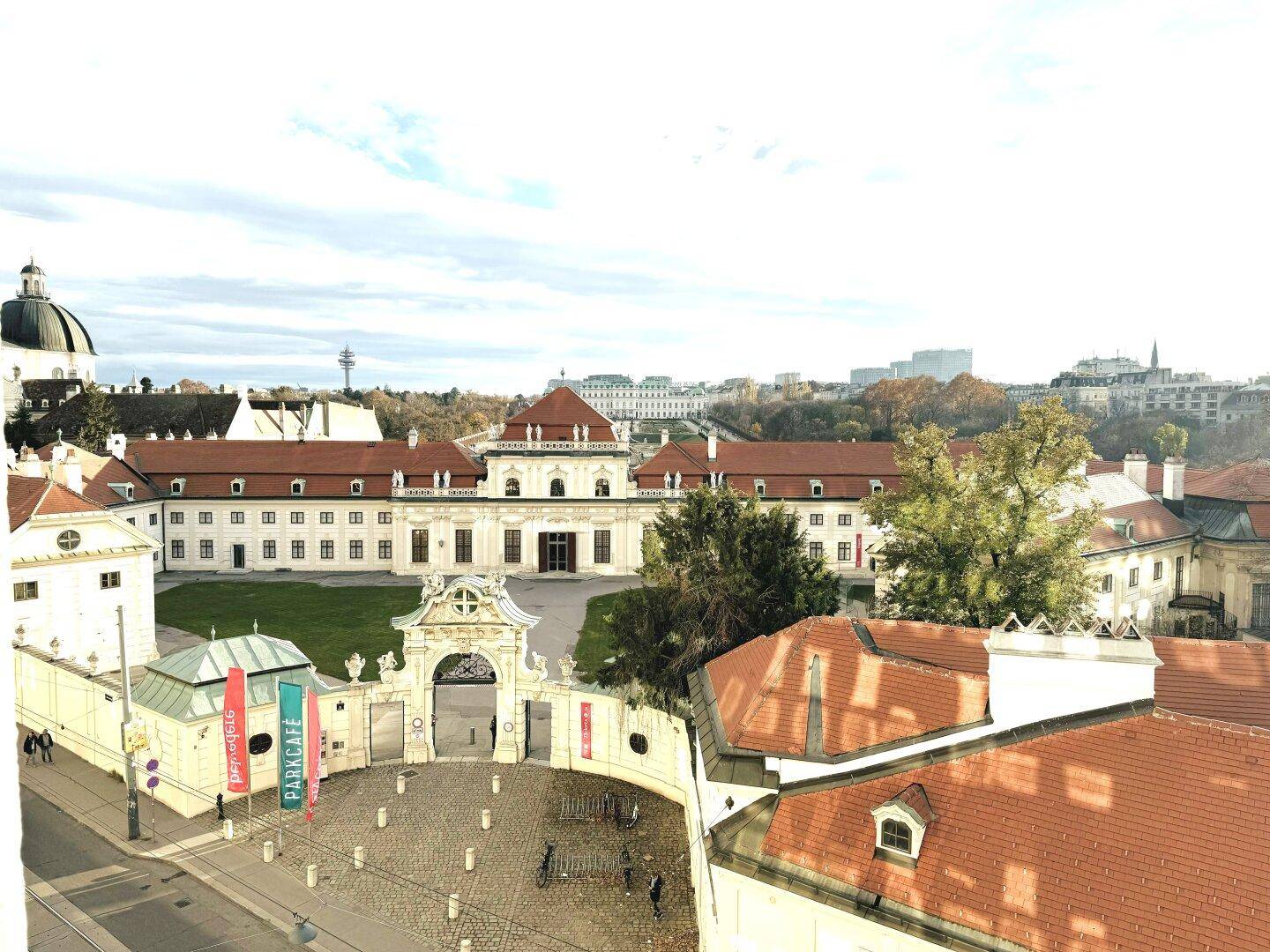 Historischer Gebäudekomplex mit einem imposanten Eingangstor und umliegenden Dächern unter bewölktem Himmel.